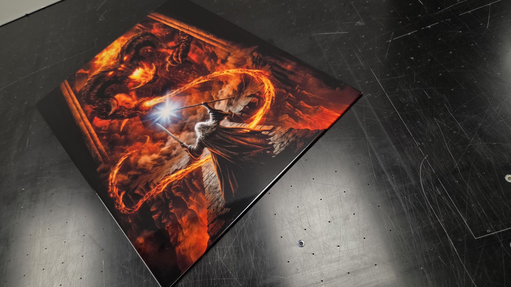 Finished Titan Forge metal panel of a wizard facing a fire demon, photographed on the workshop bench